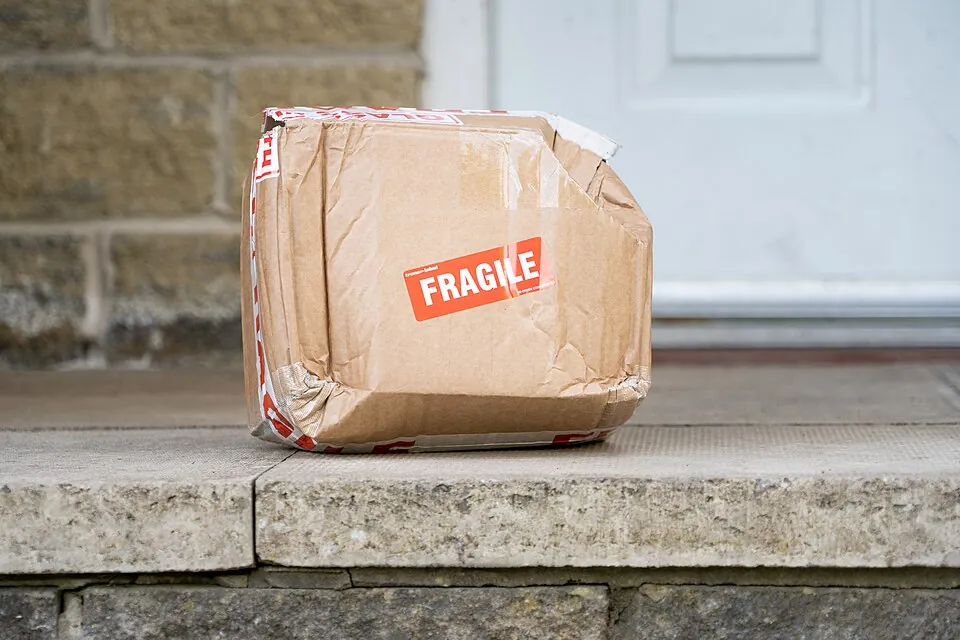 An image of a crushed cardboard box with a 'fragile' sticker on the side. The corners are misshapen and damaged and one of them has been kic