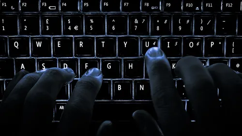 A backlit laptop computer keyboard. Most fingers are on the "home" keys for touch-typing; the 'U' key is being pressed.